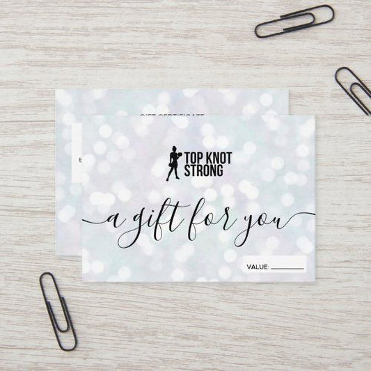 A gift card with the text "a gift for you" written on it, placed on a wooden surface with two black paper clips.